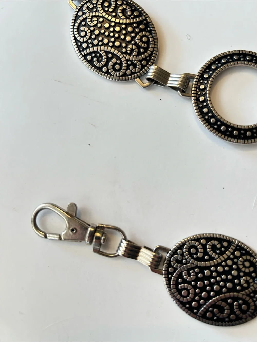 Silver-tone chain belt features textured medallion links and a hook closure L/XL